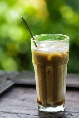 Sütlü buzlu sütlü buzlu Latte ve Koyu Ahşap Masada Büyük Bardakta Buz Küpleri, Güzel Yeşil Yapraklı Bokeh Menüsü için Soğuk Yaz İçeceği