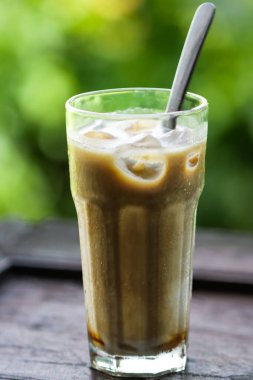 Ahşap Masa üzerinde güneş gözlüklerinin yanında kremalı buzlu kahve ve buzlu Latte, Yeşil Doğa Bokeh Mutfak Yaşam Tarzı Arkaplanı ile Yaz Kafe İçeceği