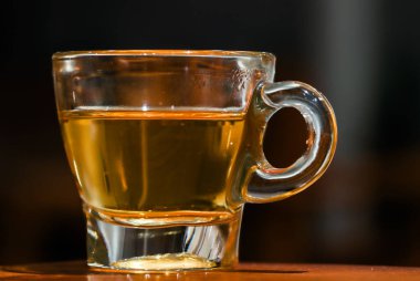 Tahta Masada Yuvarlak Saplı Zarif Cam Kupada En İyi Kaliteli Altın Çay, Koyu Bokeh Arkaplanlı Cozy Kafe İçi Sıcak Bitki İçeceklerinin Profesyonel Yakın Çekimi