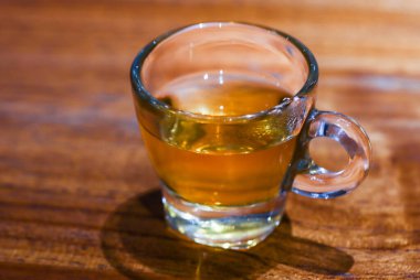 Tahta Masa üzerinde eşsiz yuvarlak saplı taze sıcak çay, Cozy Kafe Arkaplanda Yumuşak Odaklı Bokeh ile Sıcak Altın Bitki İçeceği Gastronomisi