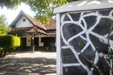 Taş Kapı ve Çamur Döşeme Çatılı Geleneksel Asya Evi, Noktalı Güneş Işığı Gölgeleri ve Düşmüş Frangipani Çiçeği ile Sahne Bahçesi