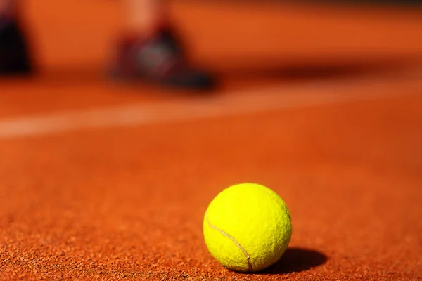 Tennisplatz mit Tennisball und Männerbeinen im Hintergrund. — Stockfoto