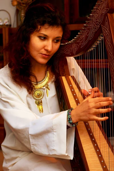 Meisje harpiste in witte jurk met juwelen die haar instrument spelen. — Stockfoto