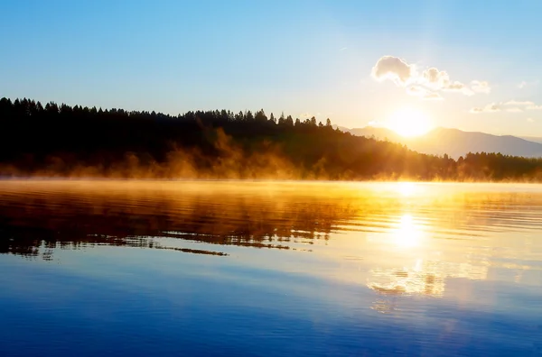 Hermoso paisaje con montañas y lago al amanecer en tonos azules y naranjas dorados . — Foto de Stock