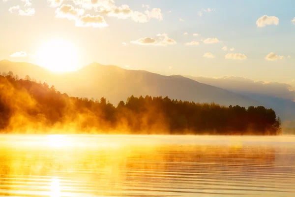 Bela paisagem com montanhas e lago ao amanhecer em tons de azul dourado e laranja . — Fotografia de Stock