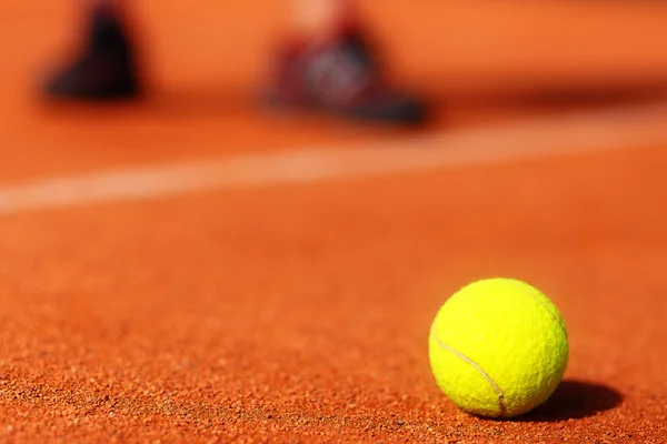 Tennisplatz mit Tennisball und Männerbeinen im Hintergrund. — Stockfoto