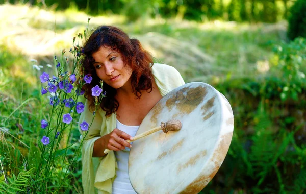 Schönes schamanisches Mädchen mit schamanischer Rahmentrommel auf Hintergrund mit Blättern und Blumen. — Stockfoto