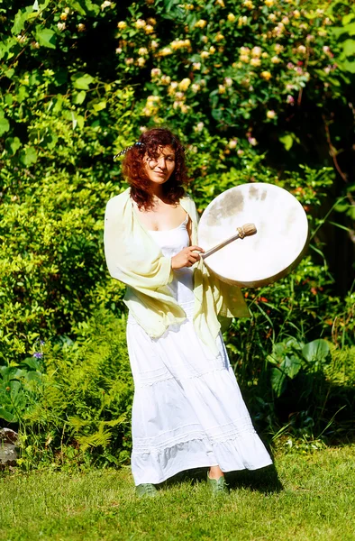 Belle fille chamanique jouant sur chaman cadre tambour sur fond de feuilles et de fleurs . — Photo