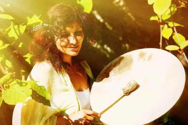 Красива шаманська дівчина грає на шаманському барабані в природі. ефект сонячного світла . — стокове фото