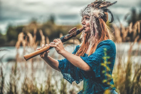 Mooi sjamanistisch meisje spelen op sjamaan fluit in de natuur. — Stockfoto