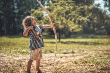 Genç bir çocuk tahta bir yayla ateş ediyor..