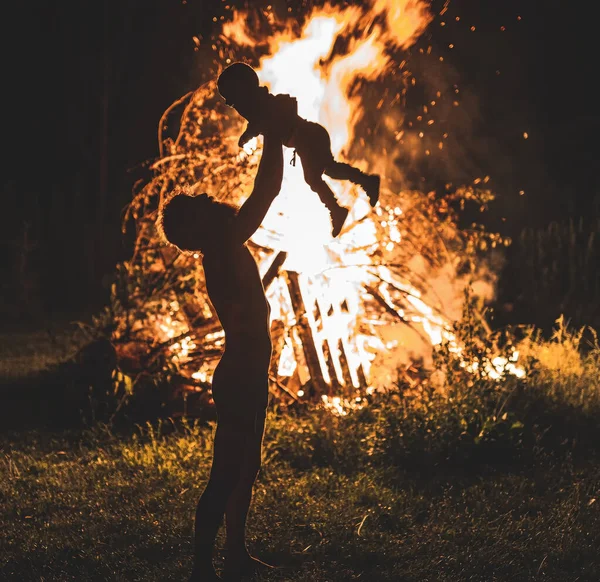 Ojciec trzymający swojego synka z płonącym ogniskiem w tle, ojcostwem i radością życia. Efekt świetlny. — Zdjęcie stockowe