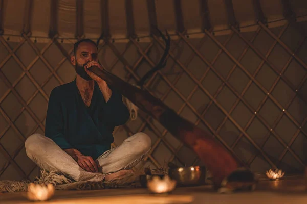 Hombre playng en didgeridoo a la luz de las velas y tazón de tibetano. —  Fotos de Stock