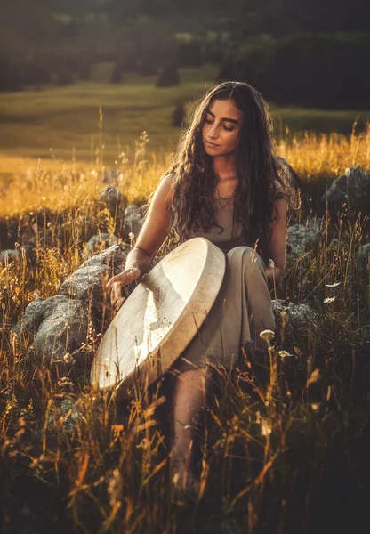 Mooi sjamanistisch meisje spelen op sjamaan frame drum in de natuur. — Stockfoto