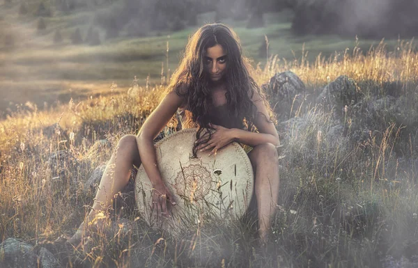 Mooi sjamanistisch meisje spelen op sjamaan frame drum in de natuur. — Stockfoto