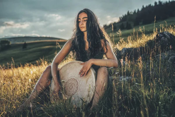 Bella ragazza sciamanica che gioca sul tamburo telaio sciamano nella natura. — Foto Stock