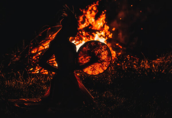 Beautiful shamanic girl playing on shaman frame drum in the nature