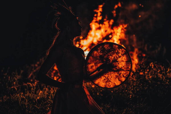Beautiful shamanic girl playing on shaman frame drum in the nature