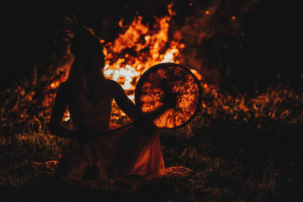 Beautiful shamanic girl playing on shaman frame drum in the nature