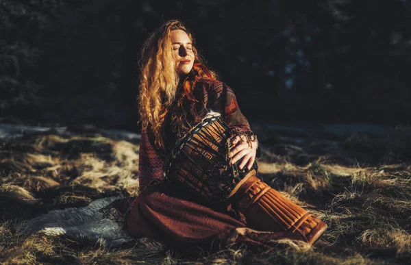 Hermosa chica chamánica tocando el tambor en la naturaleza. — Foto de Stock