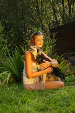 Sarı saçlı genç güzel kadın kollarında bir arka bahçe yeşil çim ile oturuyor ve sevgiyle bir sokak köpeği tutuyor