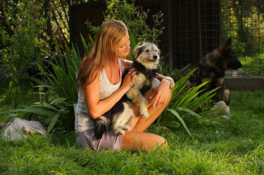 Sarı saçlı güzel bir genç kadın sevgiyle bir arka bahçesinde bulunan yeşil çim kollarında bir sokak köpeği tutuyor