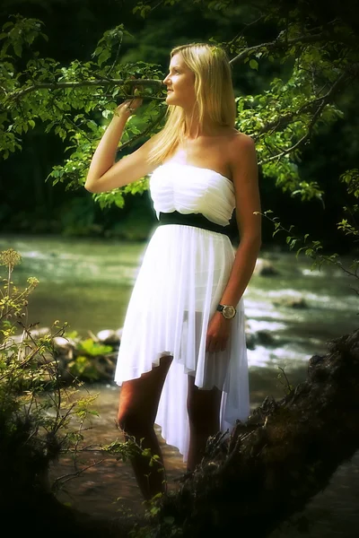 Beautiful young woman in a radiant white summer dress posing in a forest landscape with a river — Stock Photo, Image