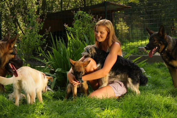 Joven hermosa mujer con el pelo rubio está sosteniendo amorosamente un perro callejero en sus brazos sentado en un jardín del patio trasero con hierba verde — Foto de Stock