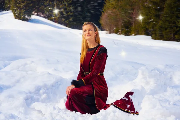 Beautiful young blonde lady in medieval velvet clothing posing in the snowy mountain landscape with fairy starlights — Stock Photo, Image