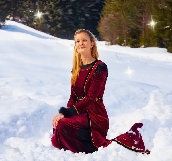 A beautiful young blonde lady in medieval velvet clothing posing in the snowy mountain landscape with fairy starlights — Stock Photo, Image