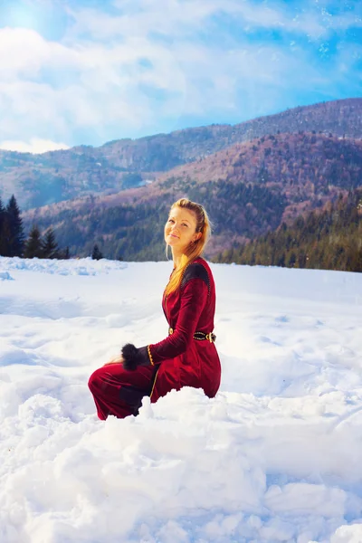 Μια όμορφη νεαρή κοπέλα ξανθιά στο μεσαιωνικό βελούδο ένδυσης θέτουν στο τοπίο χιονισμένο βουνό — Φωτογραφία Αρχείου