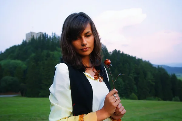 En vacker flicka i historisk kostym i en vild äng landskap håller en secretful romantisk ros i hennes händer — Stockfoto