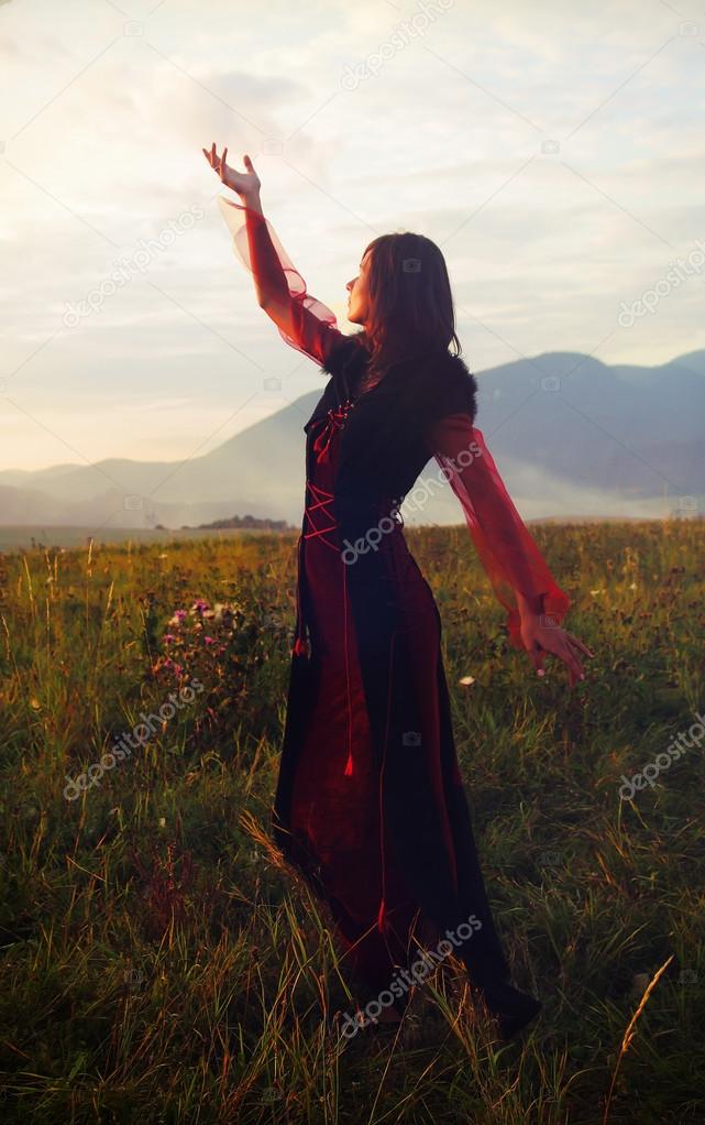 A beautiful fairy girl in a historical costume with long transparent sleeves standing amids a wild meadow landscape