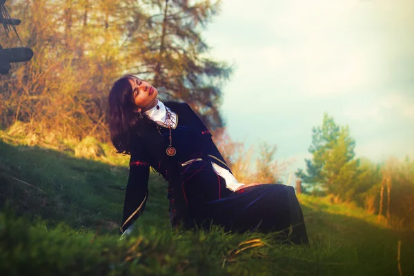 A beautiful young woman with dark hair and a historical dress posing on a meadow in open lanscape — Stock Photo, Image