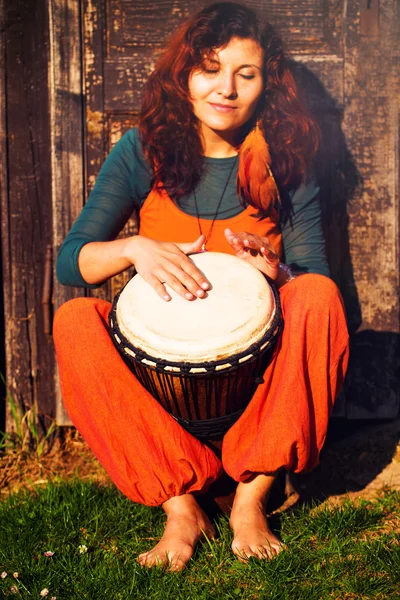 Young barefoot lady drummer playing on her djembe drum on rustic wooden door background — Stock Photo, Image