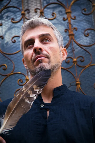 Portrait of a sexy man and eagle feathers, and ornamental medieval window on background. — Stock Photo, Image