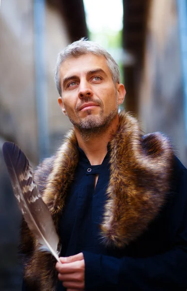 Portrait of a sexy man and wolf furry and eagle feathers, and ornamental medieval window on background. — Stock Photo, Image