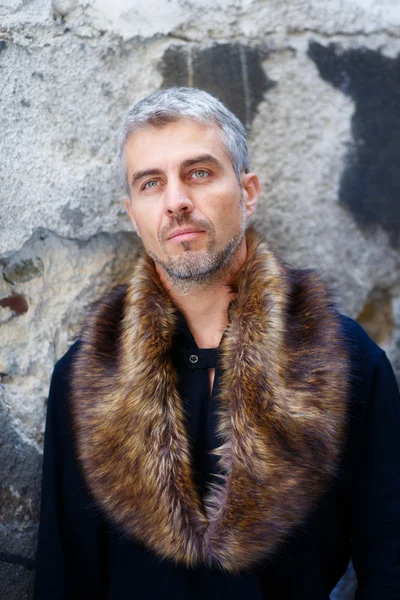 Portrait of a sexy man in wolf  fur and thoughtful expression on his face, a  structure wall on background — Stock Photo, Image