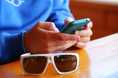 Bir restoranda oturan ve Smartphone'da oynarken gözlüklü adam.
