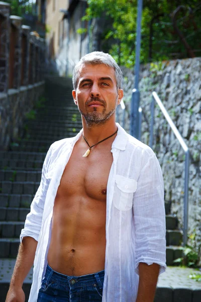 Sexy fashion portrait hot male model in stylish jeans and shirt with muscular body posing. Wolves tooth jewelery pendant. — Stock Photo, Image