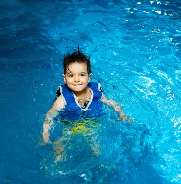 Young boy with inflatable swimming vest in the pool, has a happy smile.  Eye contact. — Stock Photo, Image