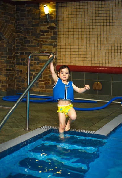 Niño con chaleco de natación inflable en la piscina, tiene una sonrisa feliz. Contacto visual . —  Fotos de Stock