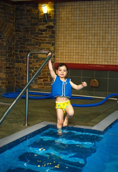 Jongen met opblaasbare vest zwemmen in het zwembad, heeft een tevreden glimlach. Contact met de ogen. — Stockfoto