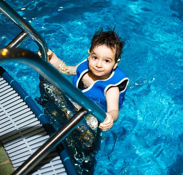 Menino novo com colete de natação inflável na piscina, tem um sorriso feliz. Contacto ocular . — Fotografia de Stock