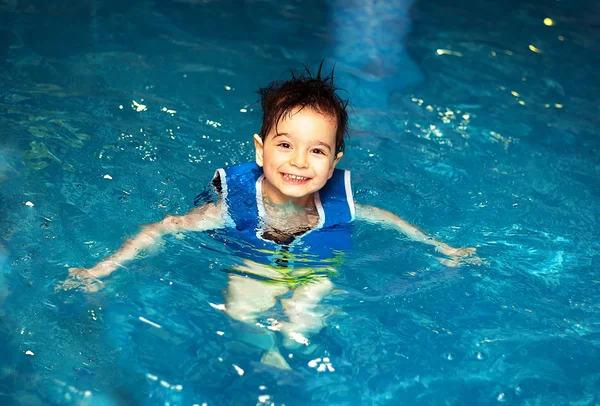 Menino novo com colete de natação inflável na piscina, tem um sorriso feliz. Contacto ocular . — Fotografia de Stock