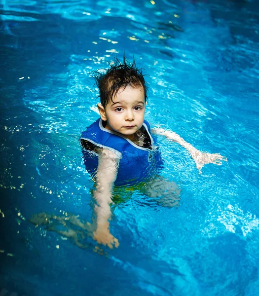 Giovane ragazzo con giubbotto gonfiabile in piscina, ha un sorriso felice. Contatto visivo . — Foto Stock