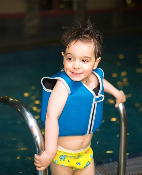 Jongen met opblaasbare vest zwemmen in het zwembad, heeft een tevreden glimlach. Contact met de ogen. — Stockfoto