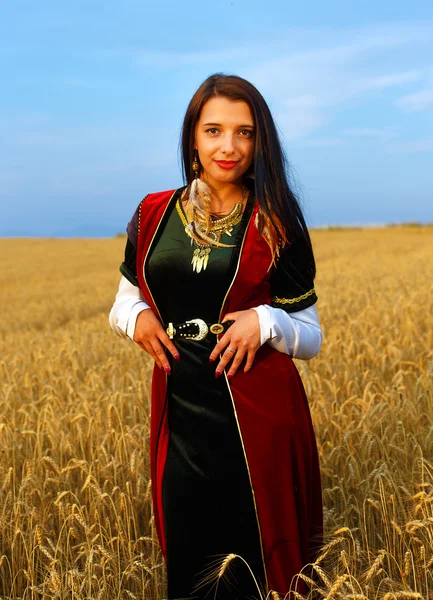 Smiling Young woman with medieval dress standing on a wheat field with sunset. Natural background. — Stok fotoğraf