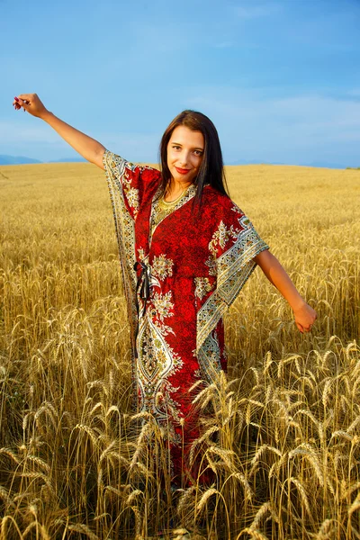 Leende ung kvinna med prydnads klänning stående på en veteåker med solnedgång. Naturlig bakgrund och blå himmel. — Stockfoto