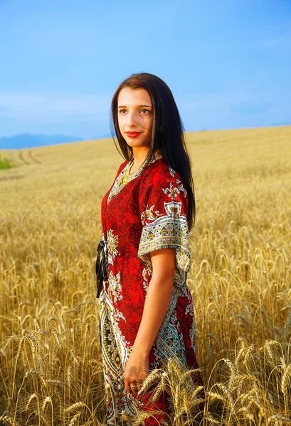 Усміхнена молода жінка з декоративним платтям, що стоїть на пшеничному полі з заходом сонця. Природний фон .. — стокове фото